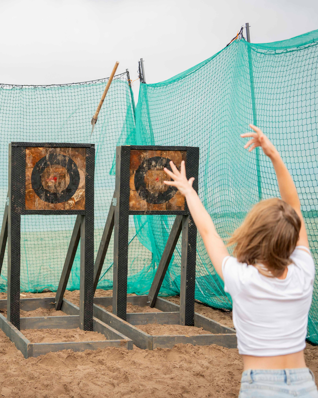 Girl throwing an axe at at an axe throwing target on the beach